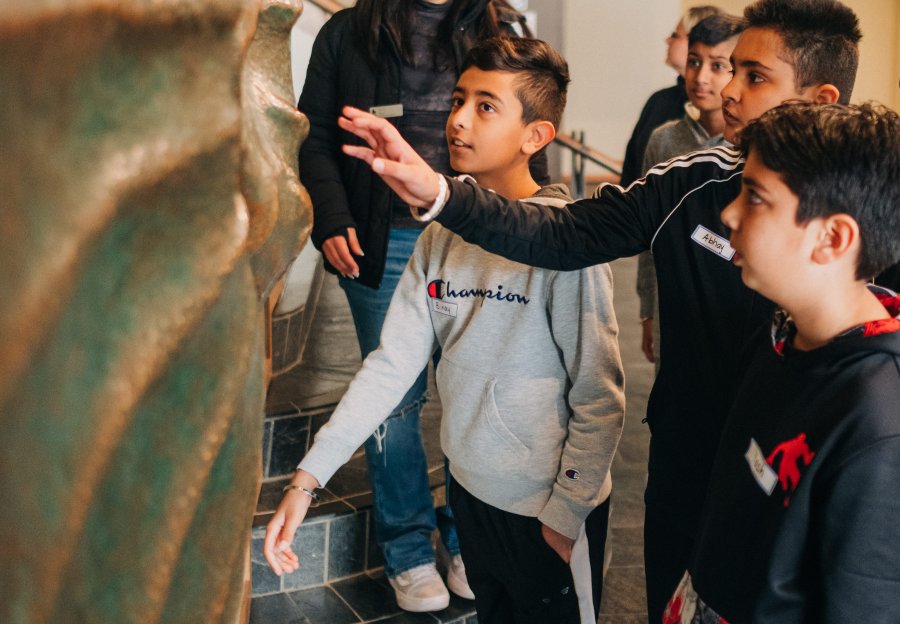 A group of students point and touch a bronze spinning sculpture in a gallery while a docent stands behind them.