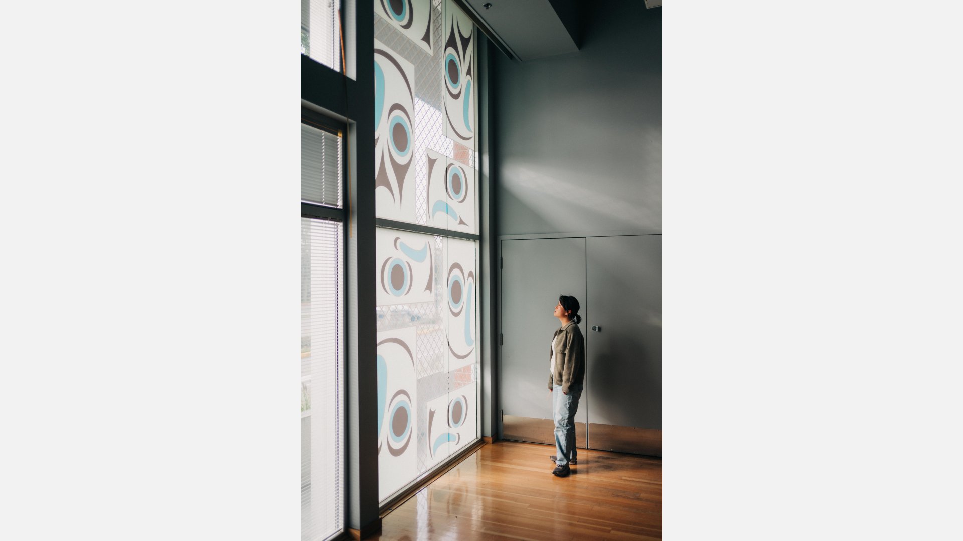 A person stands in front of a large scale window mural of eight salmon heads rendered in Salish graphic elements.