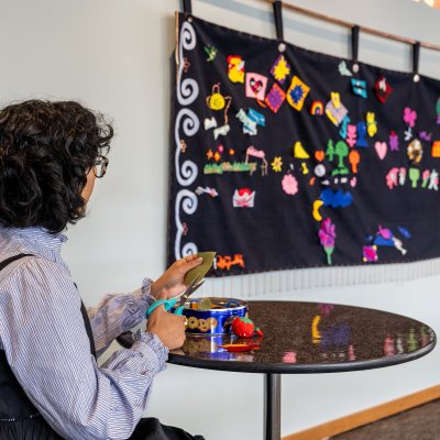 A crouching woman attaches a piece of felt to a blanket hanging on the wall.