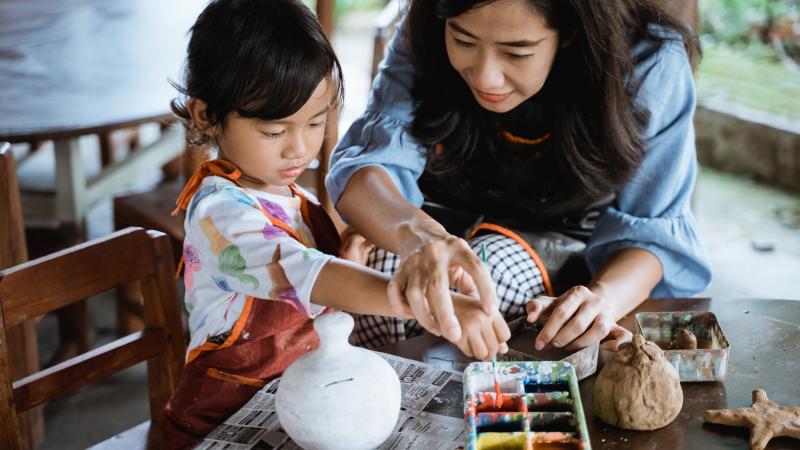Child painting a pottery piece with mom