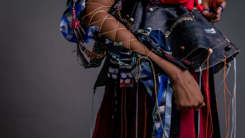 A close-up of a person with criss cross straps on their arm wearing a voluminous dress with strings dangling from it.