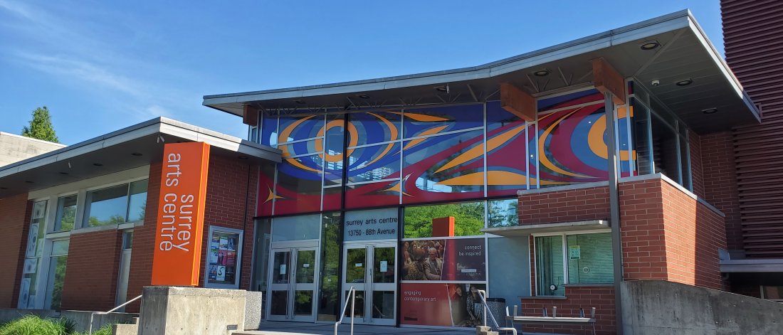 A view of the front of Surrey Arts Centre on a sunny and clear day. Atheana Picha's vinyl artwork titled "Echoes" can be seen on the windows, a work inspired by Coast Salish mountain goat horn bracelets.