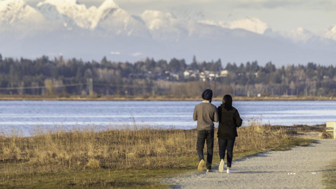 A couple walks along a gravel path in front of the water