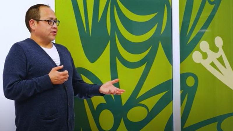 An indigenous man speaking in front of a green artwork