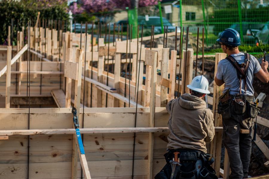 two construction workers beside a house frame