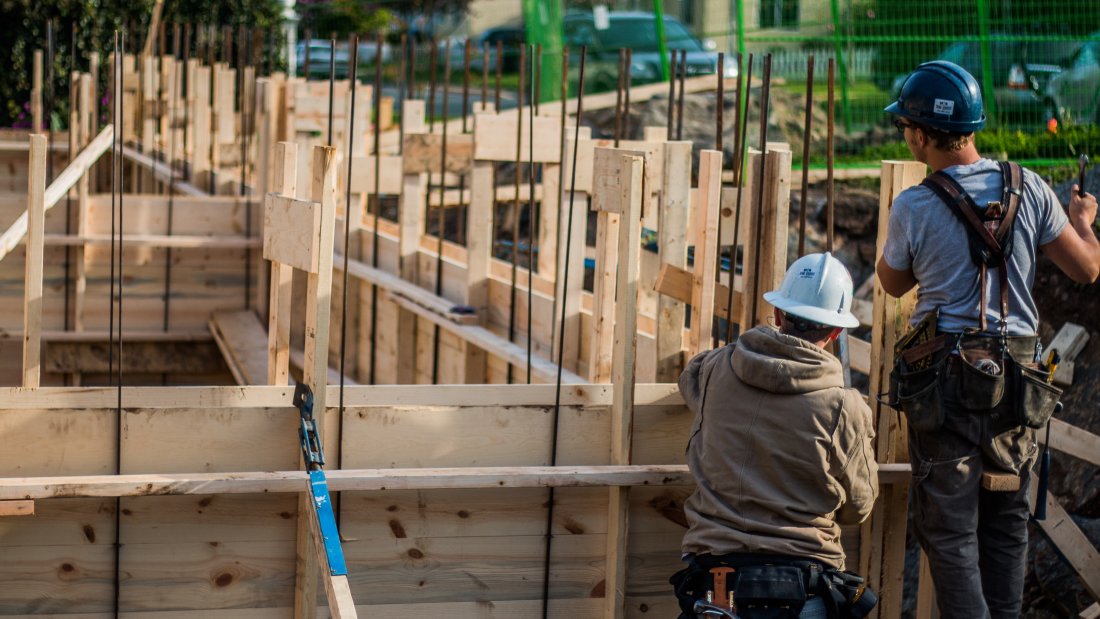 two construction workers beside a house frame