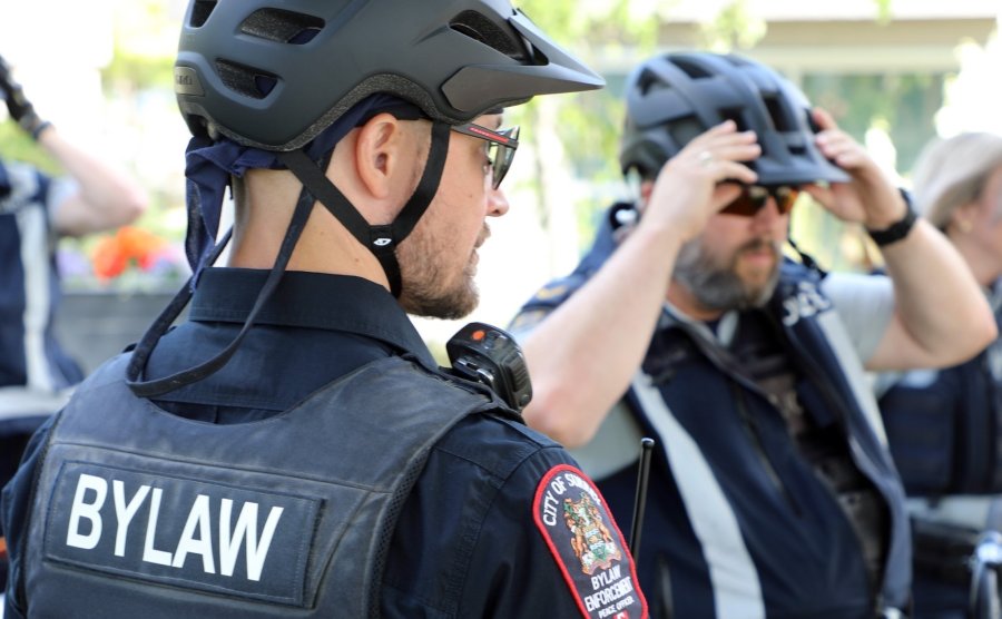 City of Surrey Bylaw Officer in uniform and helmet adjusts his radio, another officer in the background adjusts his helmet.