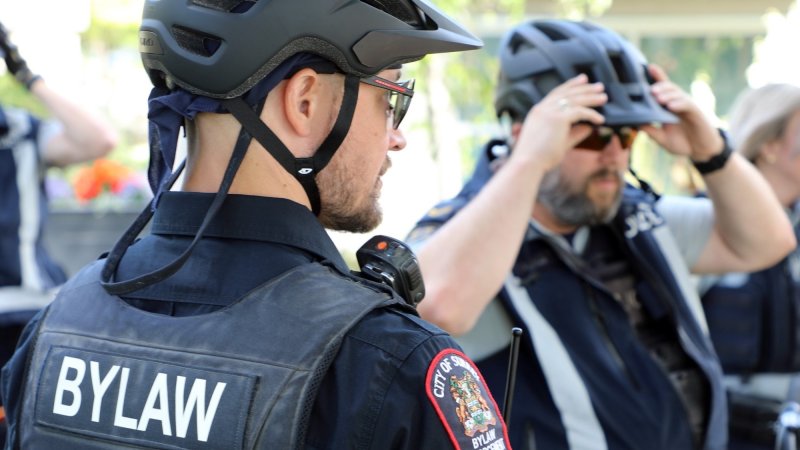 City of Surrey Bylaw Officer in uniform and helmet adjusts his radio, another officer in the background adjusts his helmet.