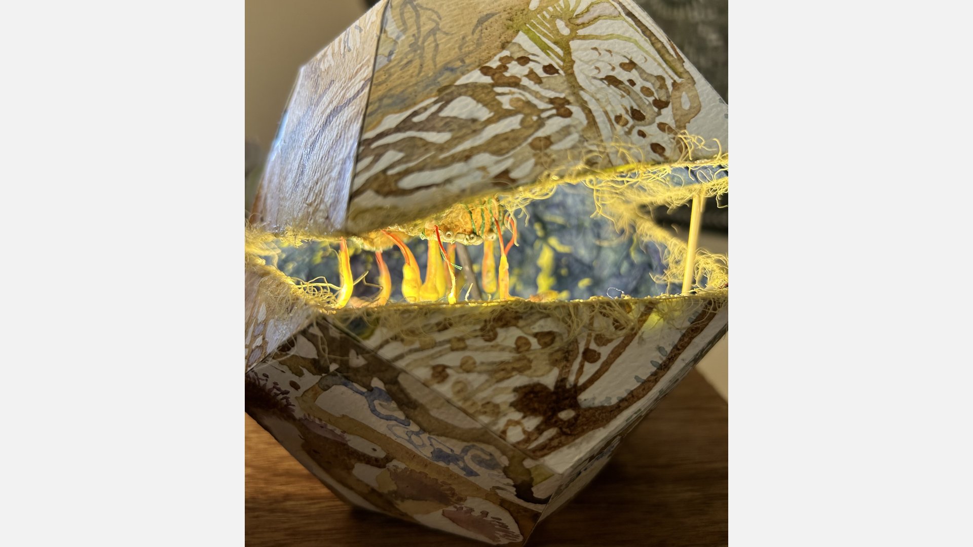 An object sits on a table resembling a shell with an opening filled with luminous strands of yellow thread.