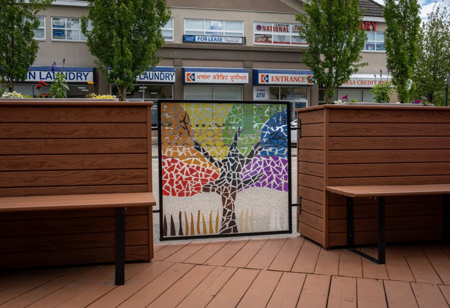 Colorful mosaic artwork on a gate in an urban outdoor seating area.