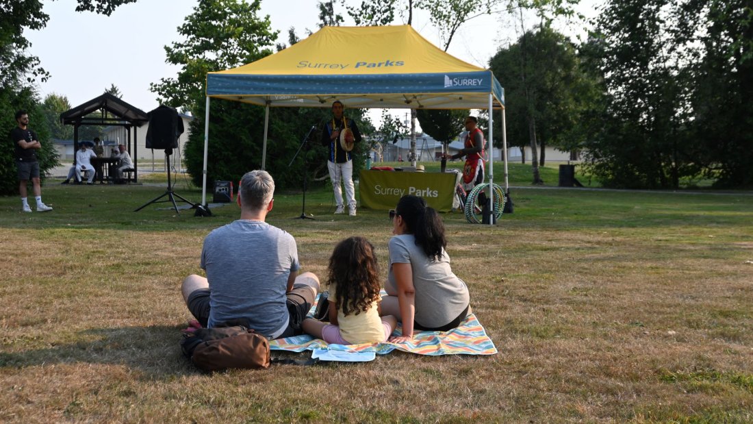family sits on a picnic blanket and watches a performance