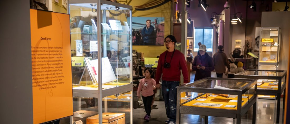 A man and a young girl explore an exhibit at the Museum of Surrey, featuring glass display cases with documents and items under dim lighting