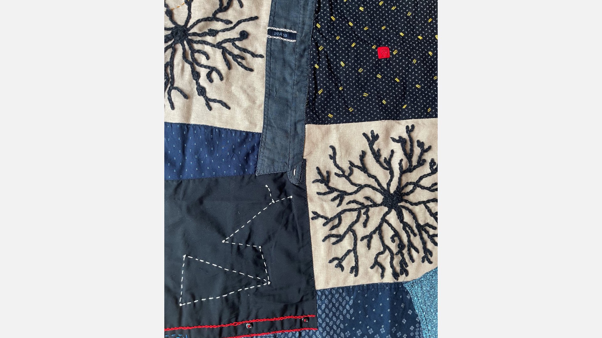 A detail of a quilt made from men's shirts, with patches of white stitching on blue and blue stitching of a web-like configuration on white.
