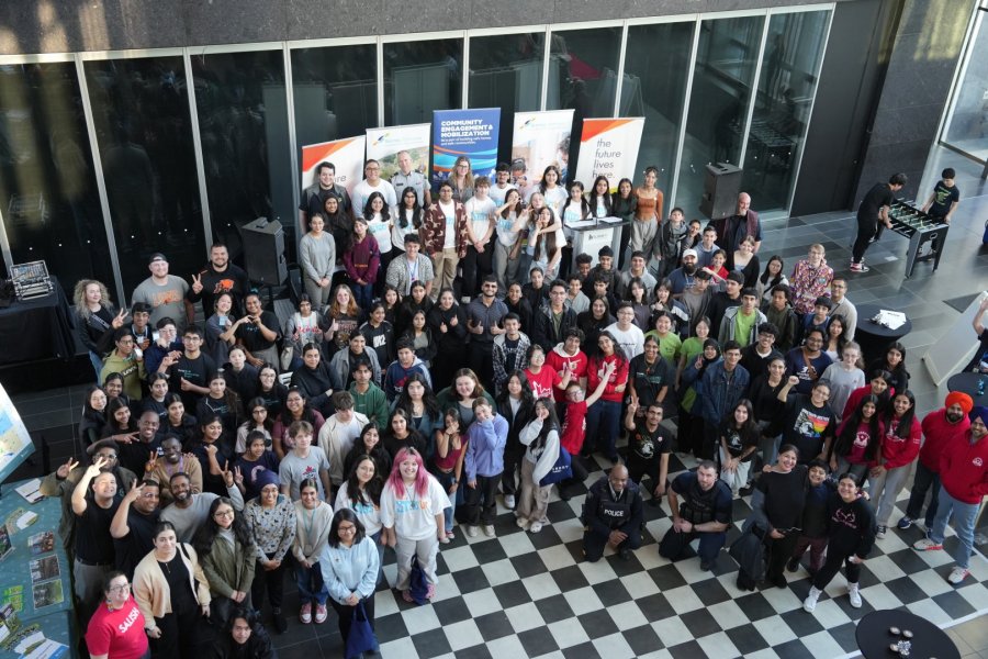 A large diverse group of people posing for a photo in an indoor setting with informational banners in the background.