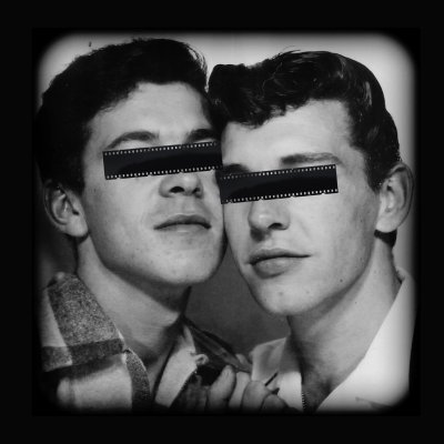 Black and white photograph of two men, their eyes covered over by celluloid tape