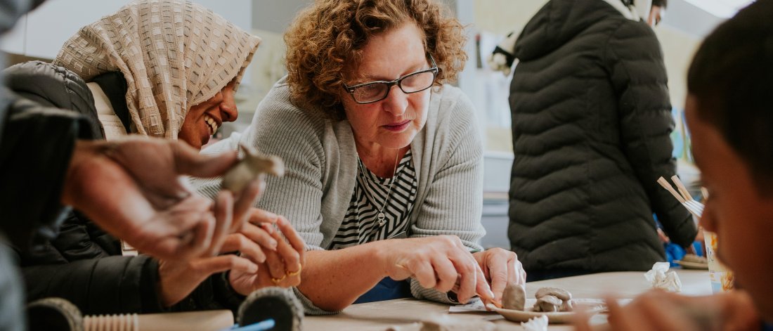 Three people are seated around a table making clay creations.