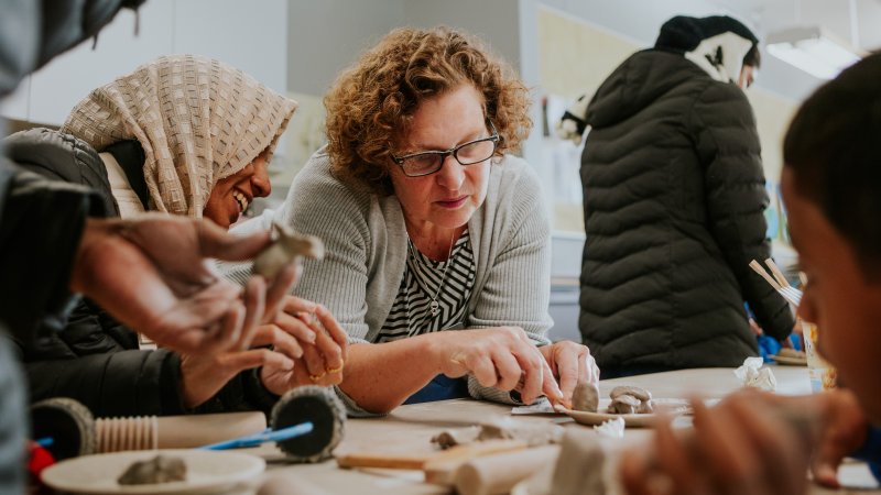 Three people are seated around a table making clay creations.