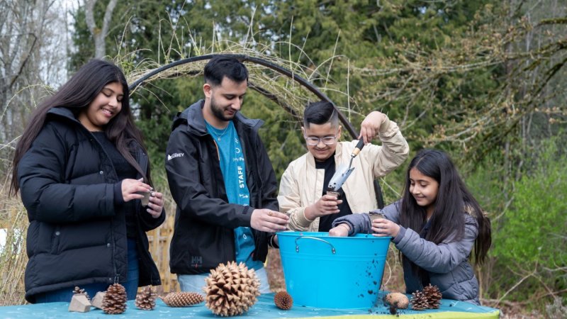 A group of children and a staff member engage in a hands-on planting activity at Darts Hill Garden during a Family Day event.