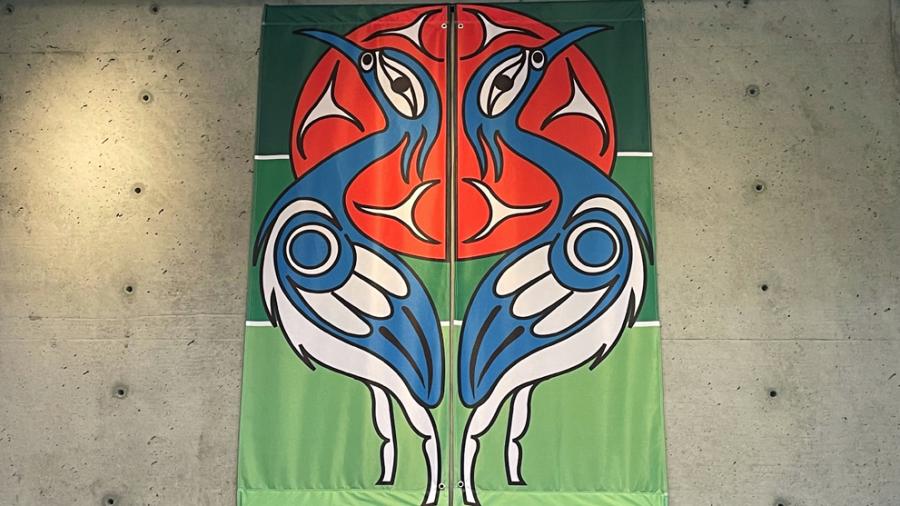 A great blue heron stands in profile against a red sun and green background on a cloth banner, with the mirror image on a banner beside it