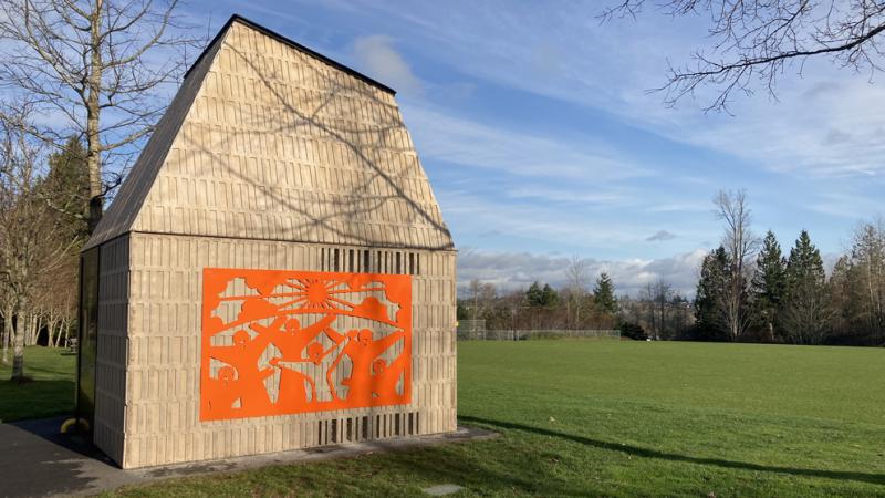 An orange artwork on the outside wall of a park washroom