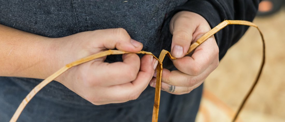 A close up of hands weaving cedar
