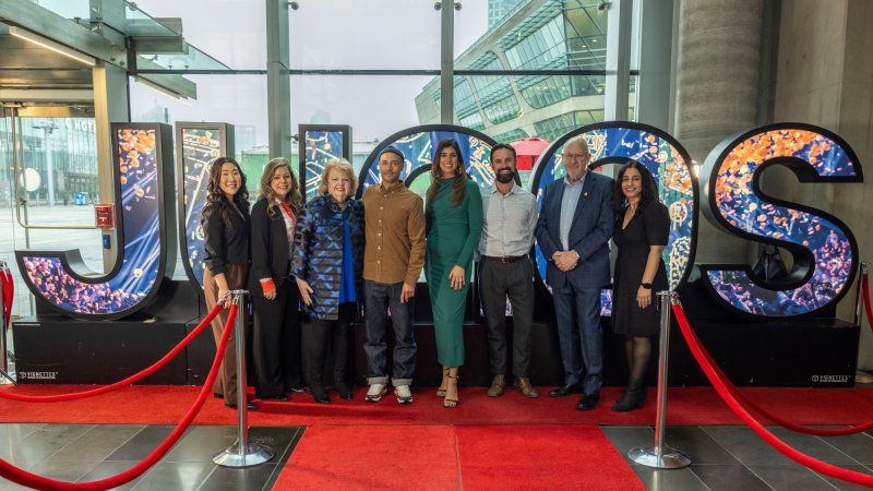 A group posing on a red carpet in front of large illuminated "JUNOS" letters at an indoor event.