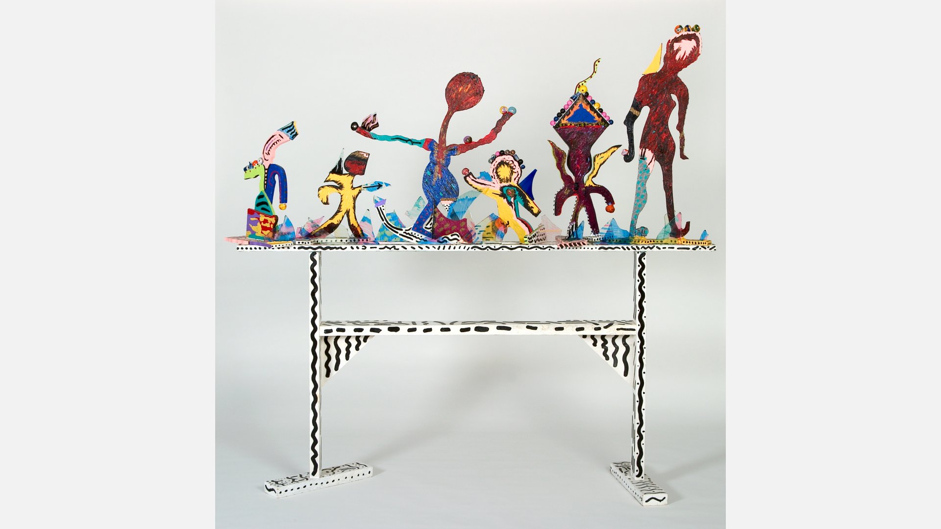 Six abstract sculptures of people displayed on a white stand with black painted details.
