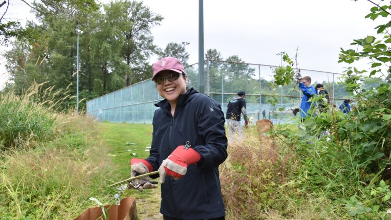 A volunteer cutting a blackberry stem into a yard waste bag.