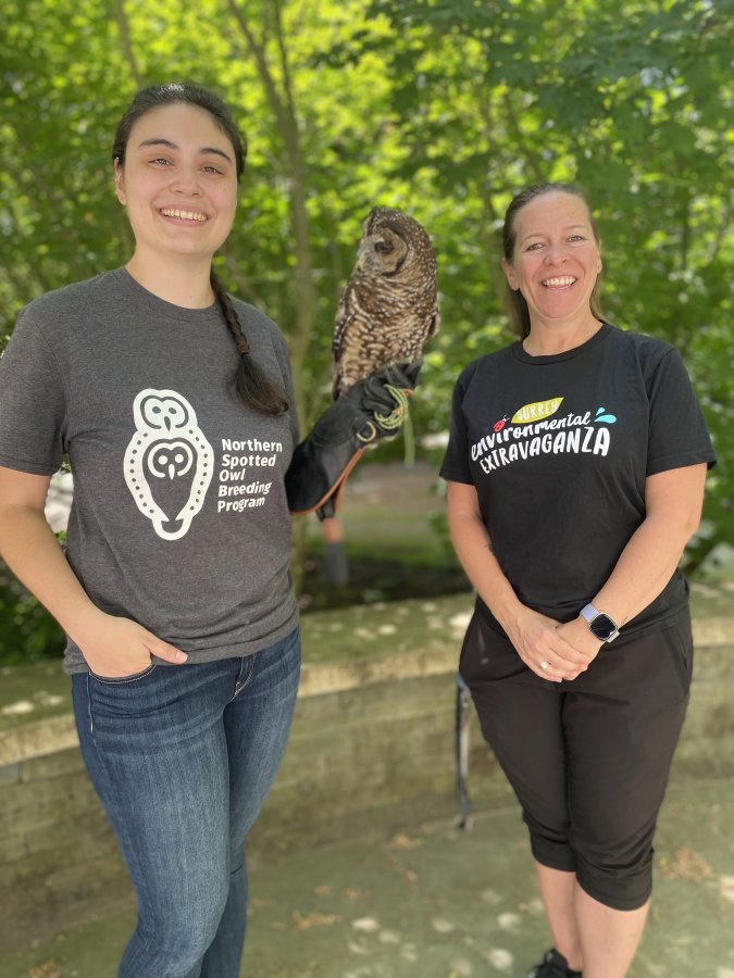 Two smiling educators, one holding a spotted owl.