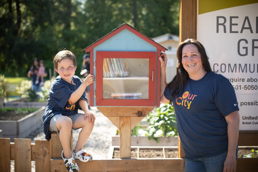 a woman and child pose beside a mini library box