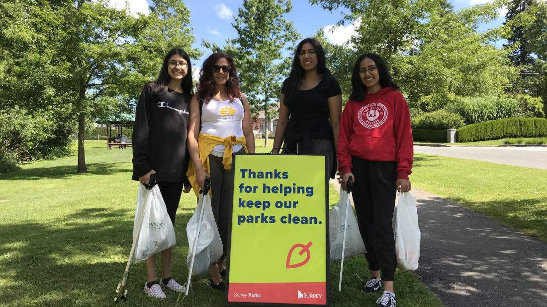 Four volunteers with litter pickers and garbage bags next to a sign.