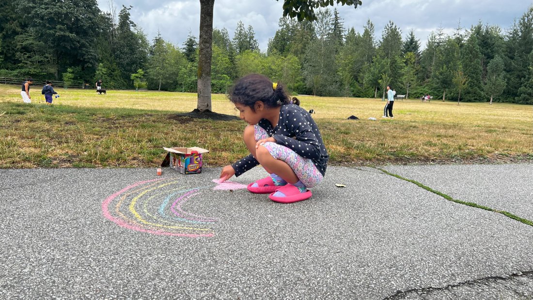 a girl draws a rainbow in chalk on a park path