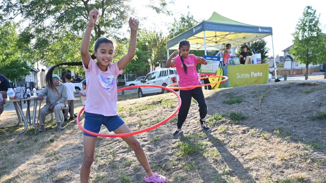 two girls hula hoop in front of a park play tent