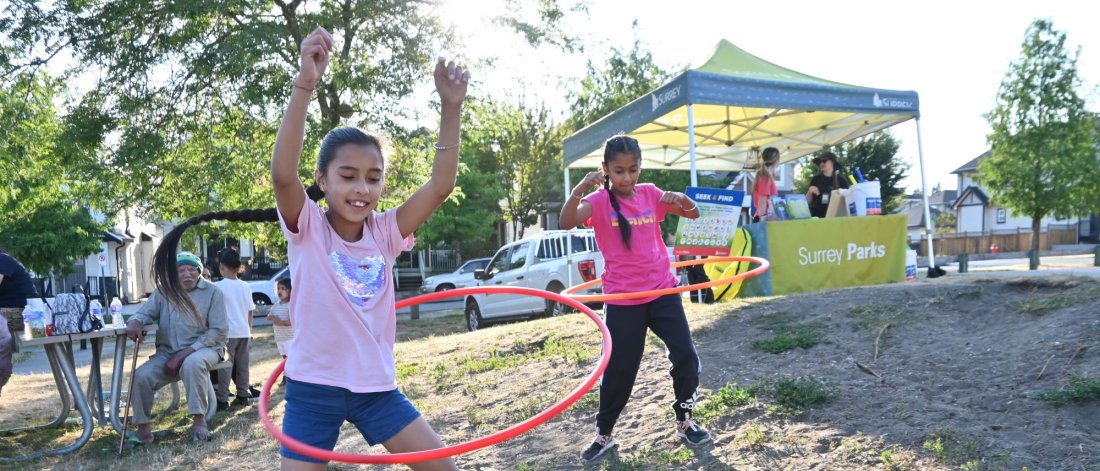 two girls hula hoop in front of a park play tent