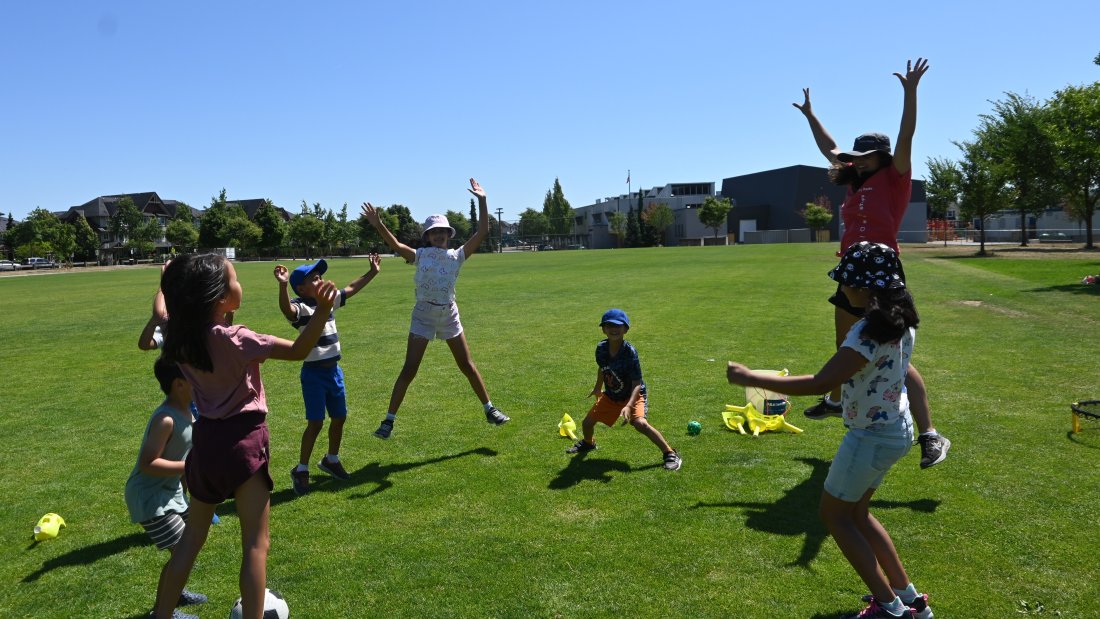 children do jumping jacks in a circle, led by a program leader
