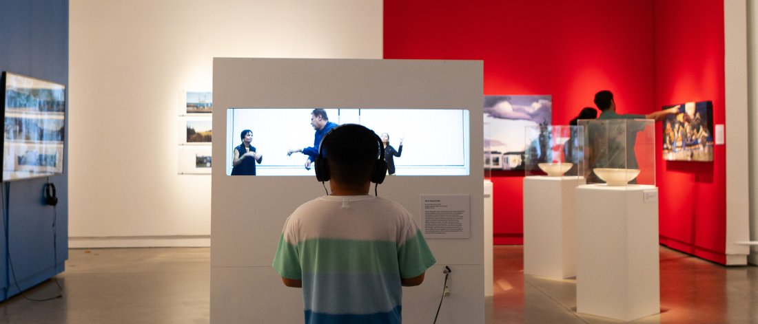 A child stands in front of a video artwork in a gallery space, with two other people in the background looking at artworks.