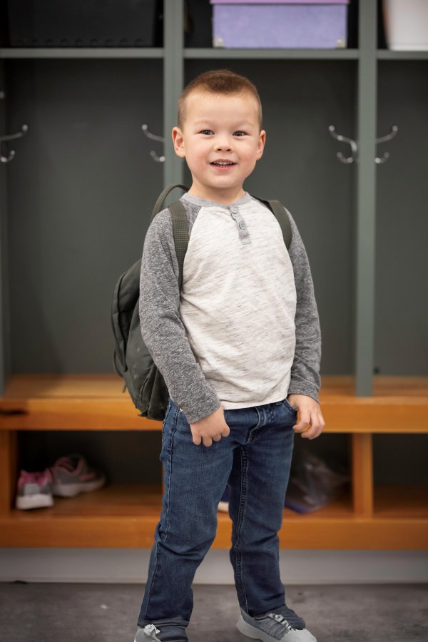 A child standing near the cubby at preschool.