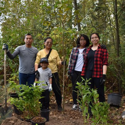 family of five holding shovel and standing next to newly planted tree