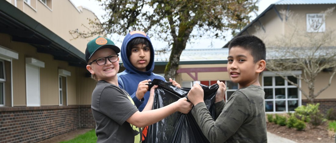 three students hold up a garbage bag
