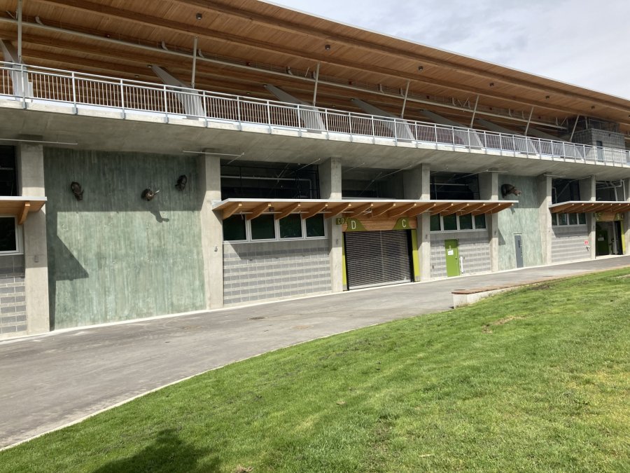Exterior of a modern community building with concrete walls and wooden overhangs, showing labeled entrances..