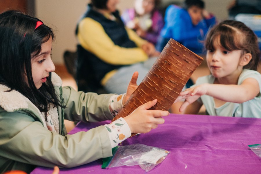 Two elementary school students touch a slab of cedar bark, marvelling at its texture.