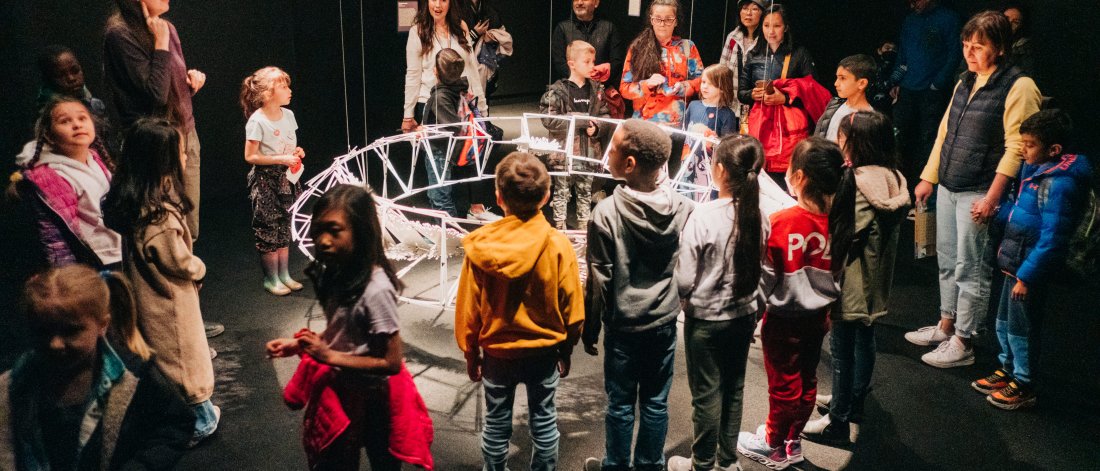 A classroom tour surrounds a space-like artwork while an artist-educator speaks. 