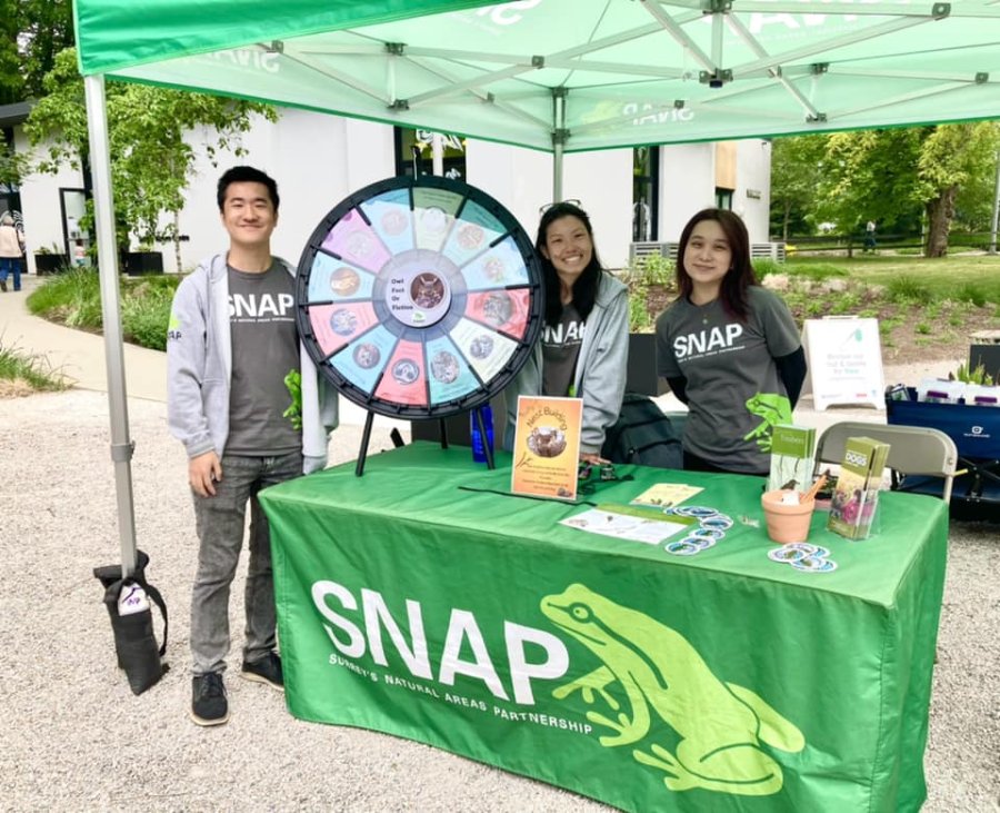 Three volunteers at an outreach booth featuring a prize wheel and educational materials.