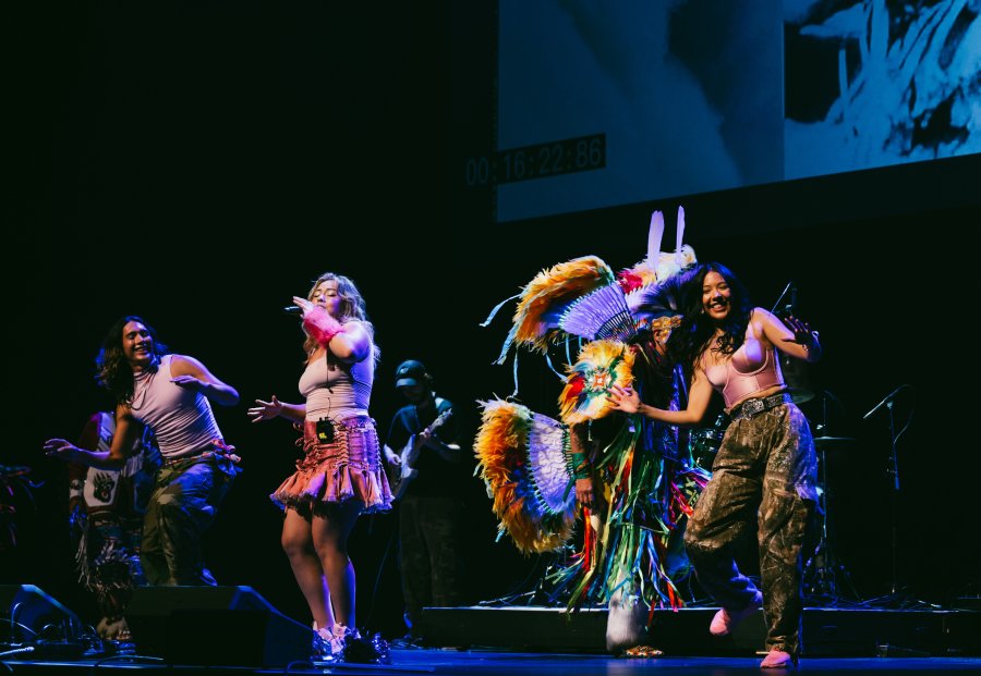 performers singing and dancing on stage, one person in colourful regalia