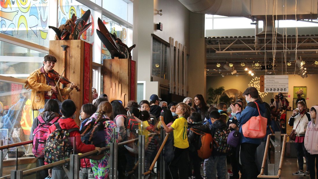 Musician playing the fiddle to a crowd of children at the Surrey Arts Centre