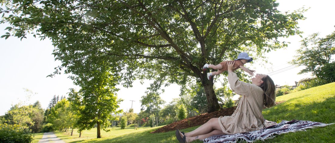 mother sitting on a picnic blanket holding baby up in the air