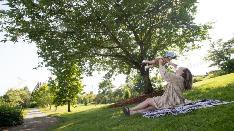 mother sitting on a picnic blanket holding baby up in the air