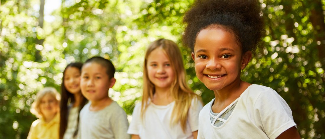 five children standing in a line with forest behind them