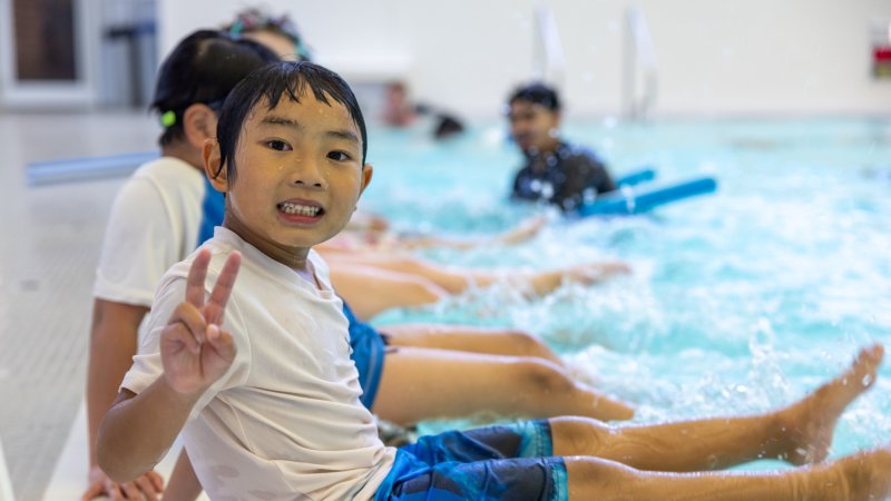 a boy is sitting at the side of an indoor pool