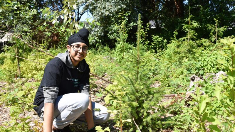 Youth volunteer next to tree.